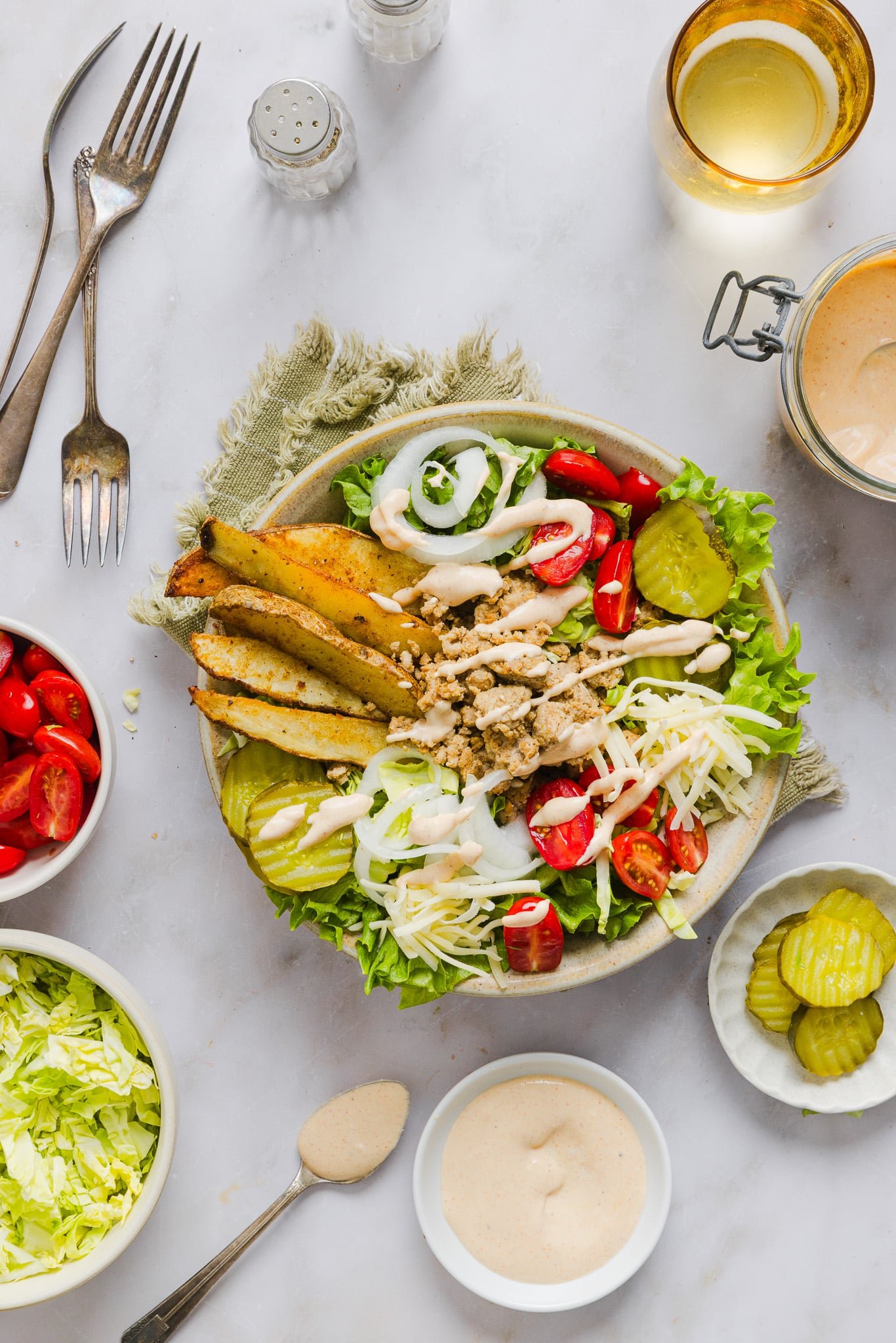 Loaded turkey burger bowl with potato wedges and veggies drizzled with burger sauce, additional veggies in small bowls on the side.