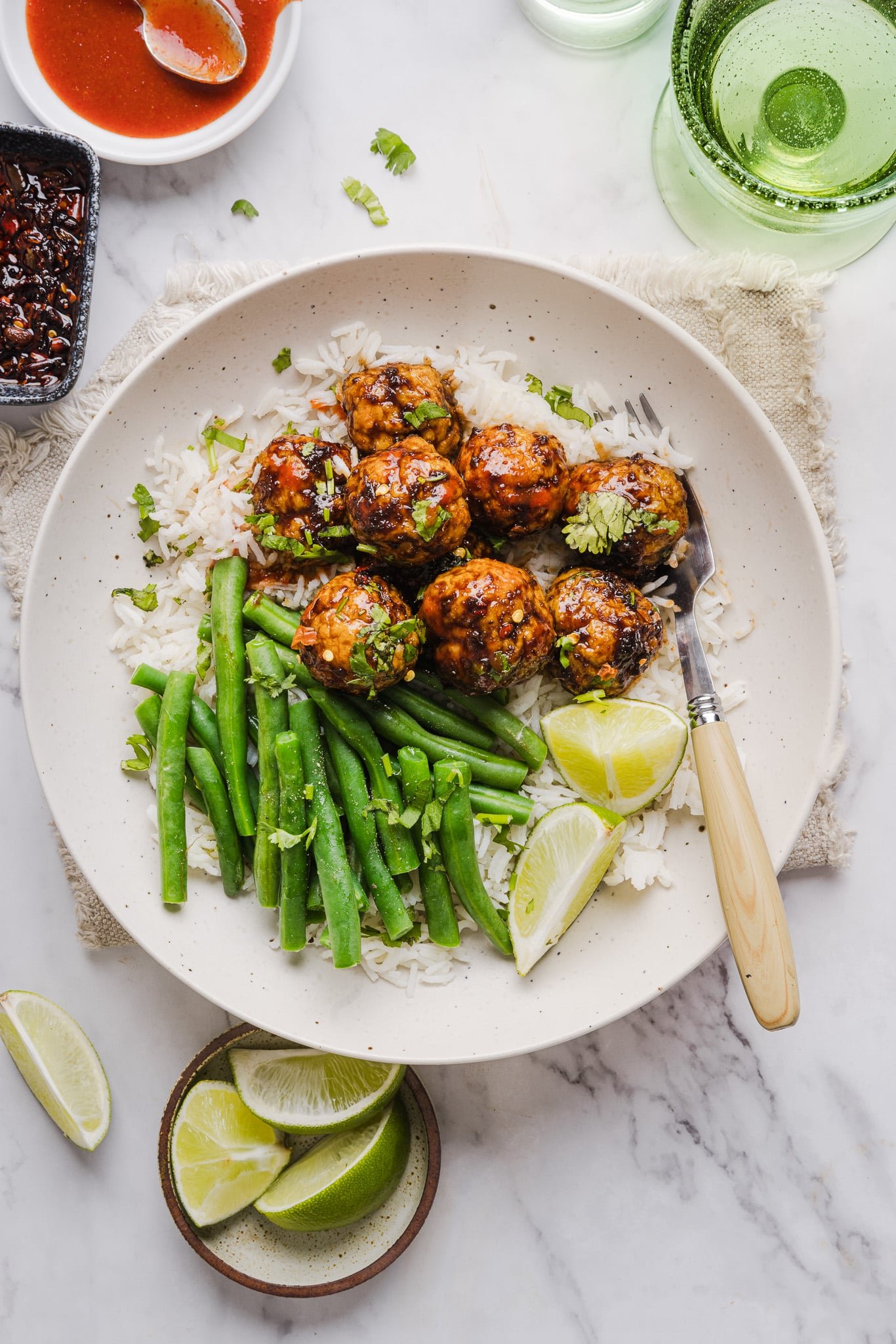 Firecracker chicken meatballs with sauce in a bowl over rice garnished with lime wedges and fresh cilantro.