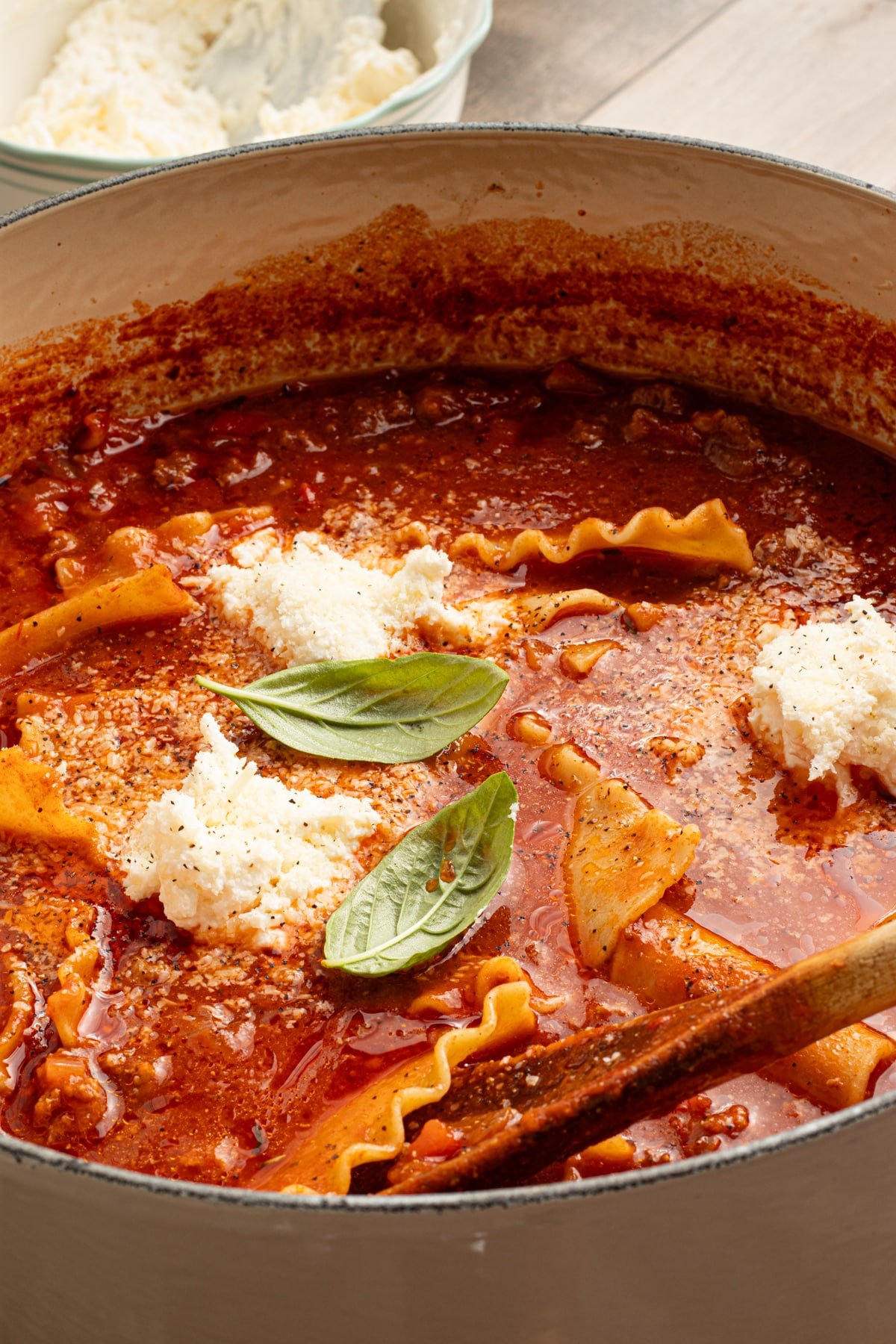 High protein lasagna soup in a large dutch oven garnished with fresh basil and cheese topping.