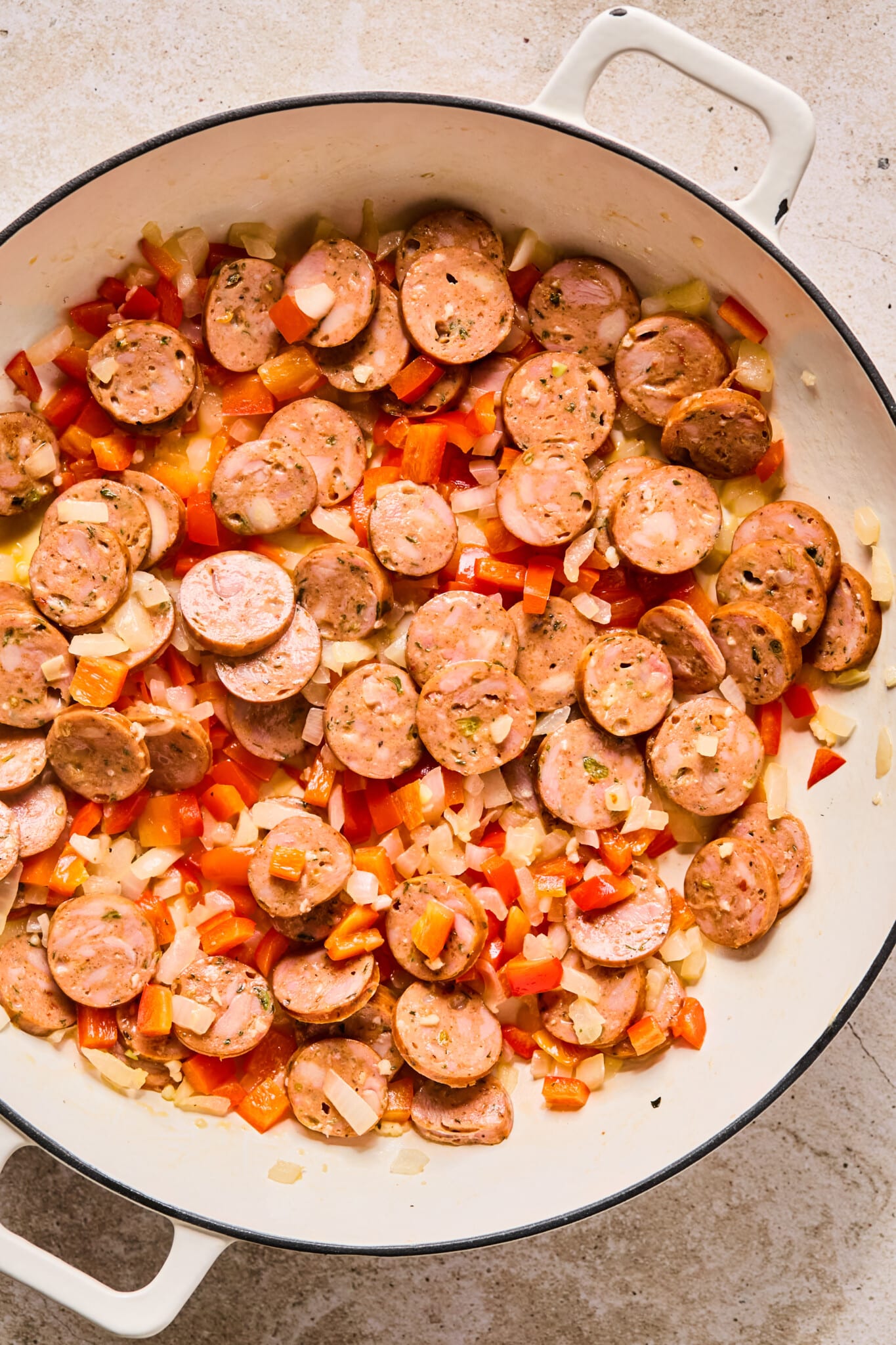 Onions peppers and garlic being sautéed with chicken sausage in a skillet.
