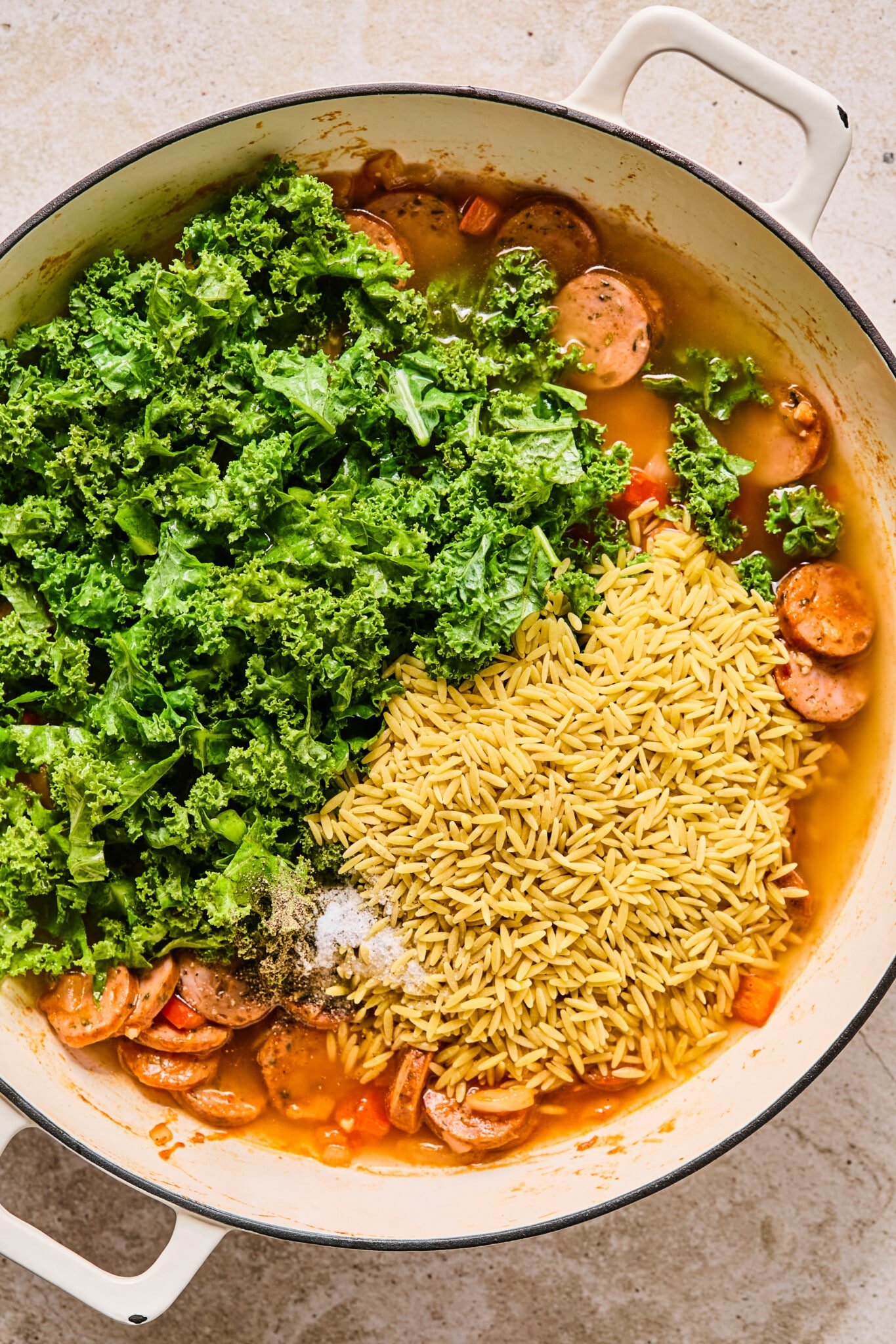 Orzo and kale being added to chicken sausage and sautéed veggies.