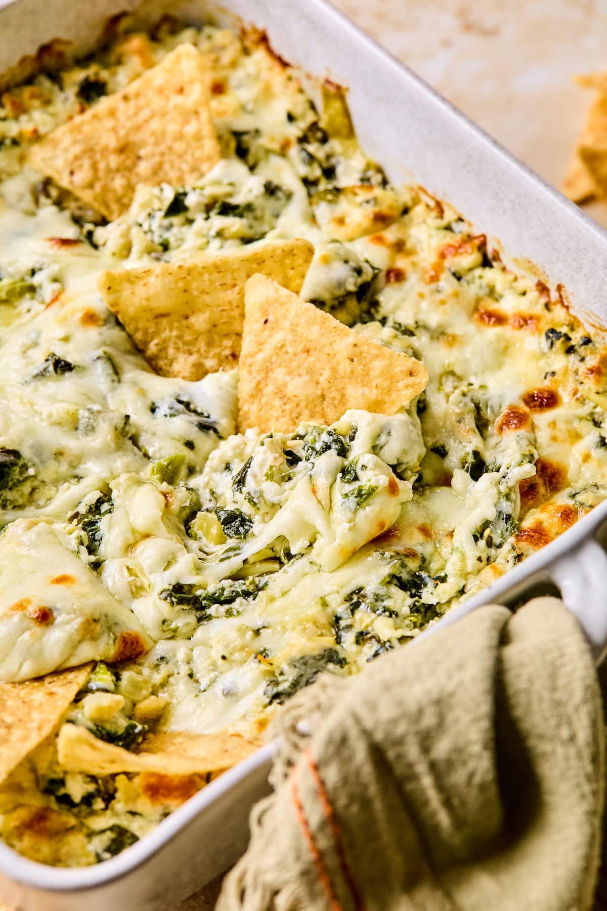 Baked cottage cheese spinach artichoke dip in a dish with tortilla chips.