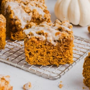 A slice of healthy pumpkin coffee cake on a baking rack with a glaze on top.