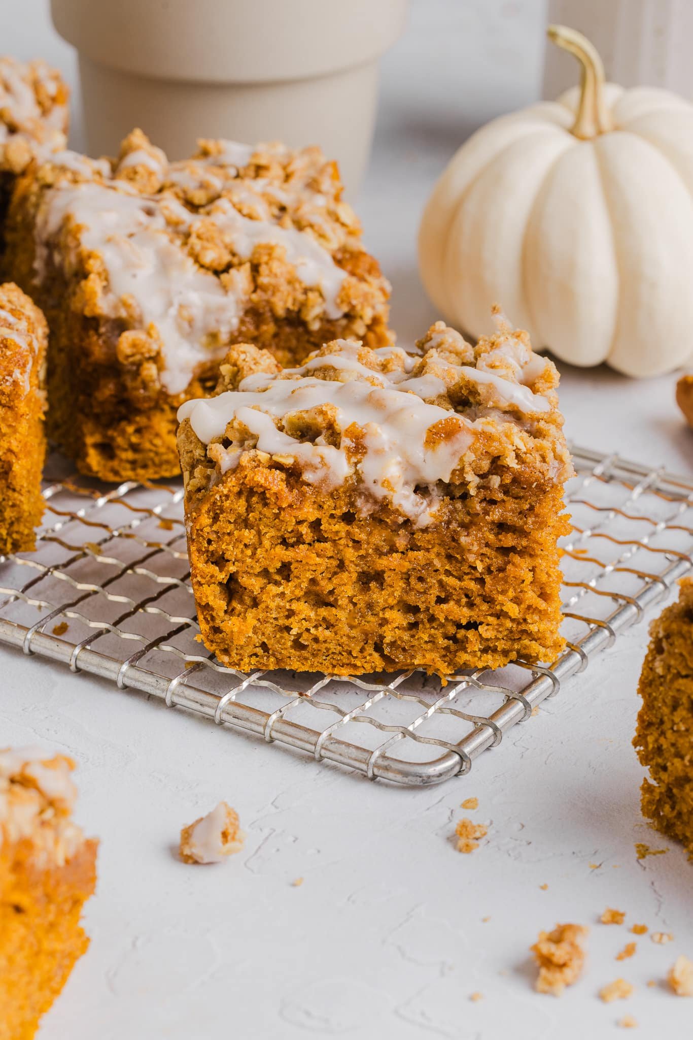 A slice of healthy pumpkin coffee cake on a baking rack with a glaze on top.