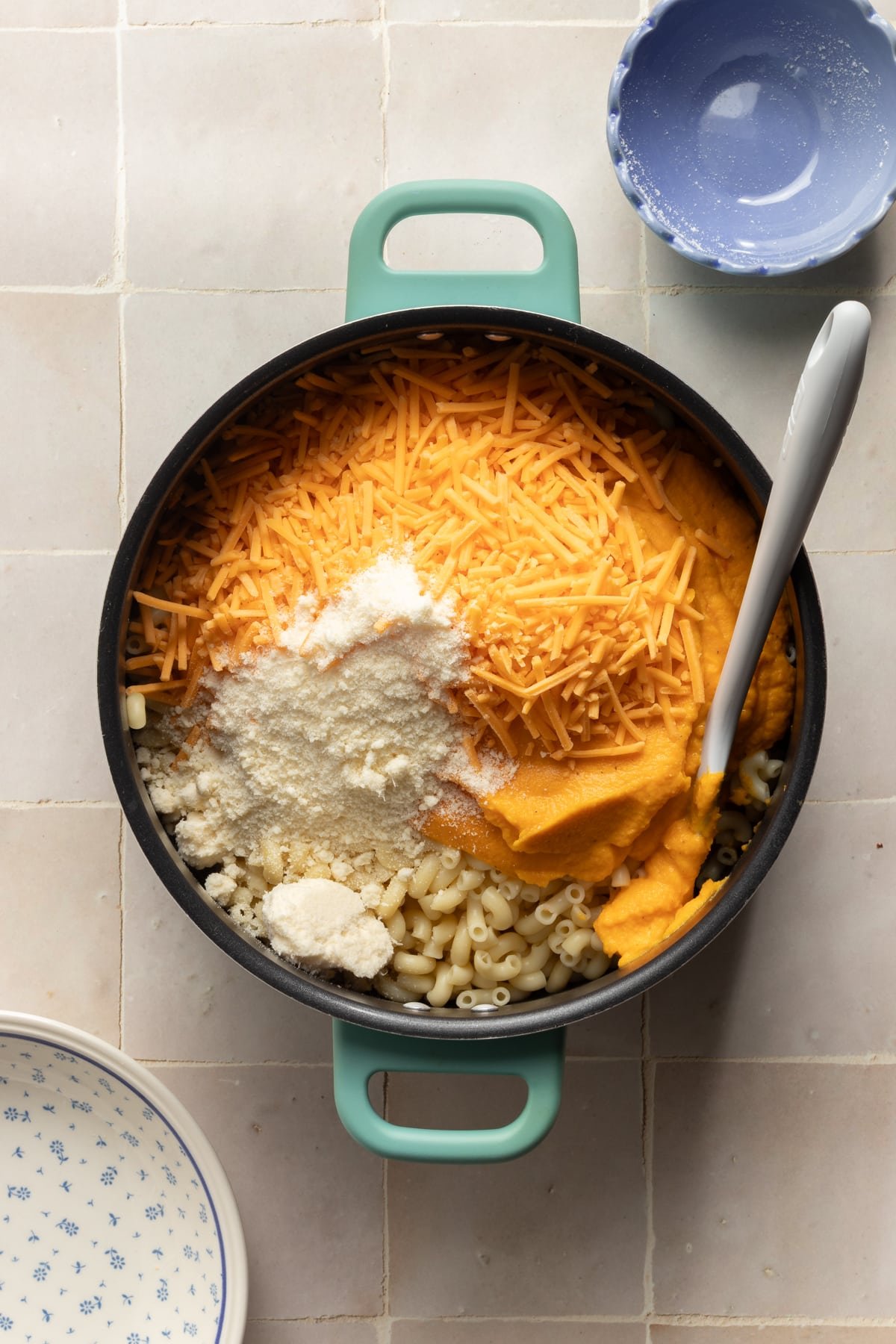 Blended veggies, cheese, and parmesan cheese being added to cooked pasta.