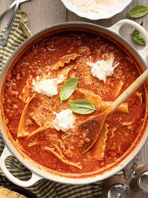 High protein lasagna soup in a large dutch oven garnished with fresh basil and cheese topping and a wooden spoon.