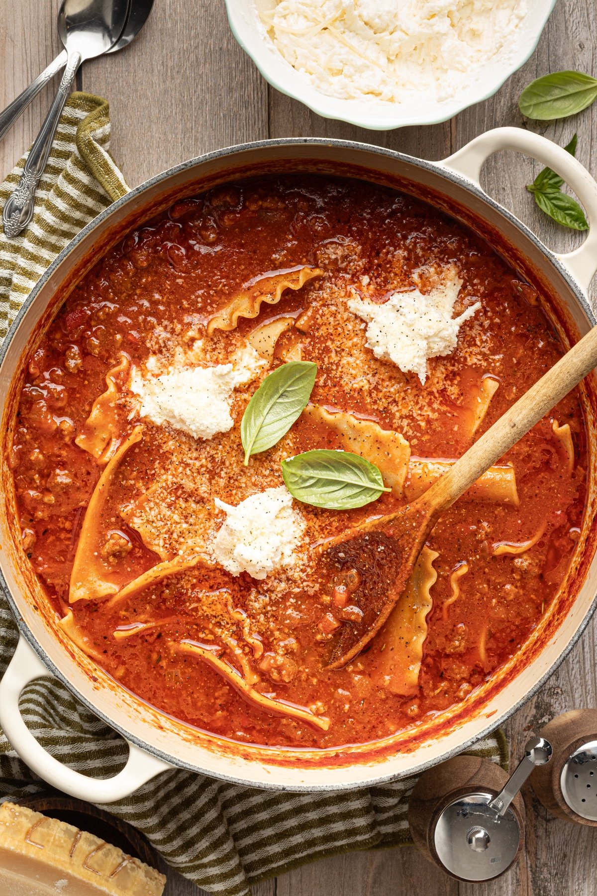 High protein lasagna soup in a large dutch oven garnished with fresh basil and cheese topping and a wooden spoon.