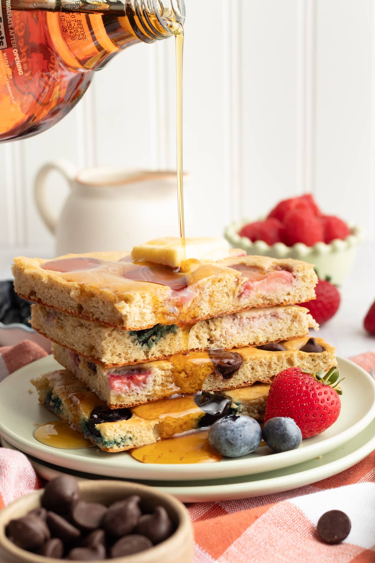 A stack of sheet pan protein pancakes with maple syrup being poured on top.