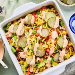 Big mac casserole topped with pickles, diced onion, tomatoes, cheese and a drizzle of sauce.