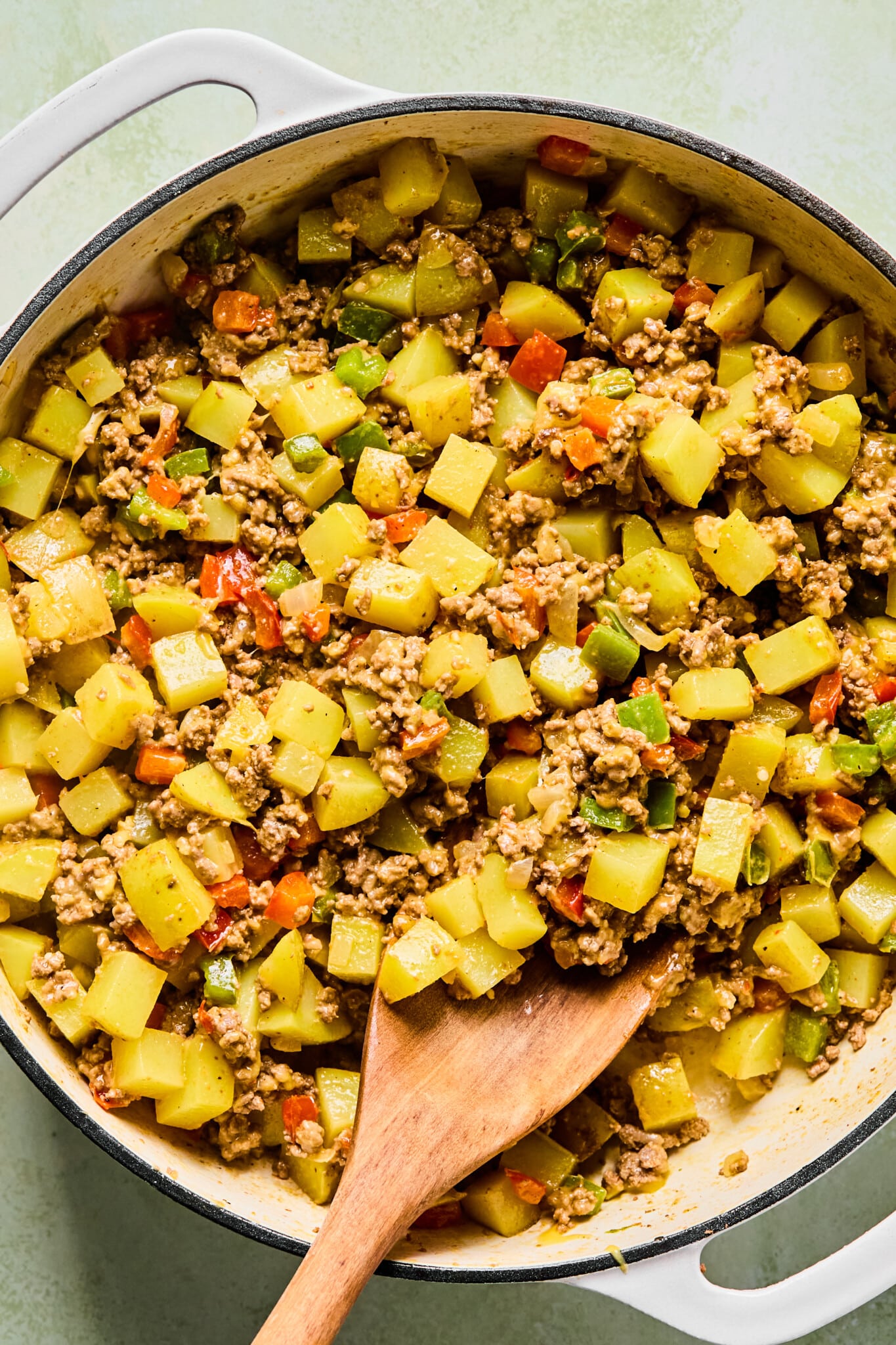 Big mac casserole in a dutch oven with a wooden spoon, ready to be transferred to a baking dish.