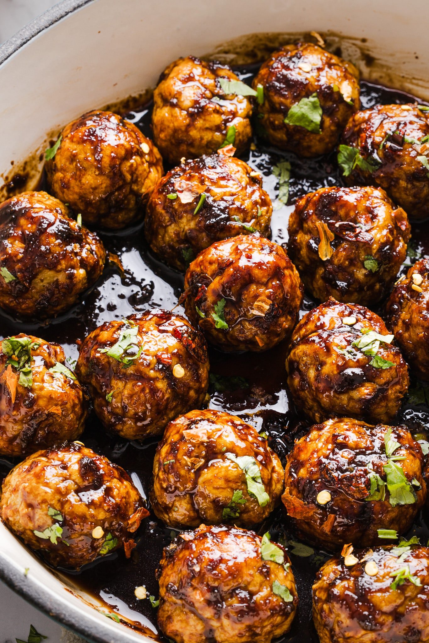 Firecracker meatballs in a pan with sauce and topped with herbs.