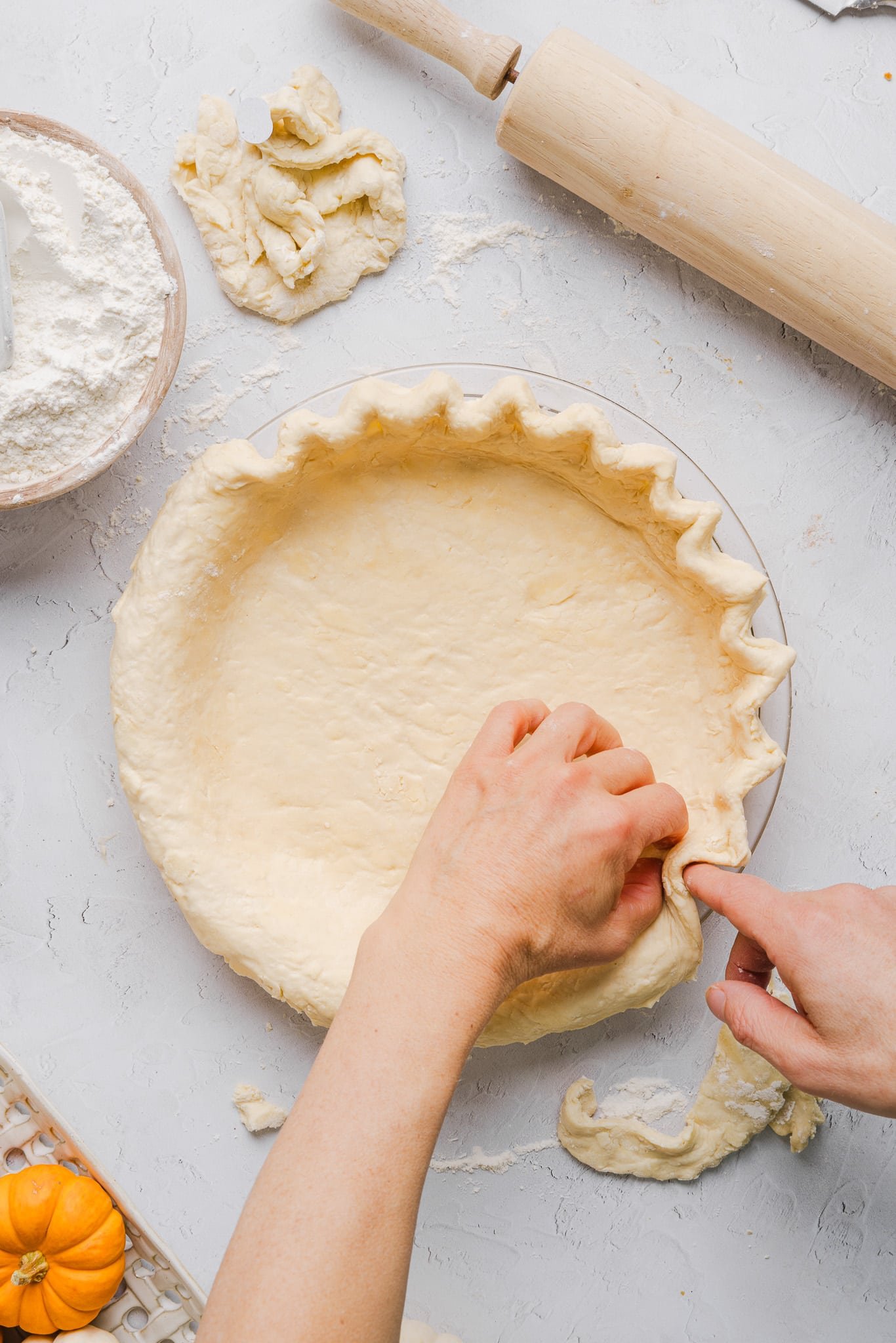 Healthy pumpkin pie crust being added to the pie pan and edges being crimped.