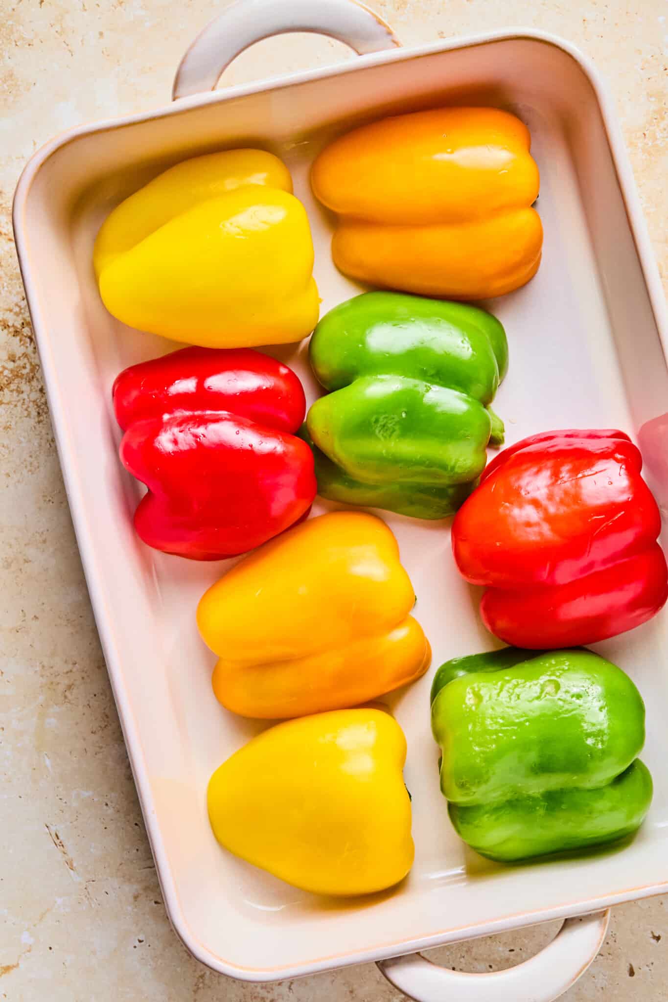 Colorful bell pepper halved, cut side down in a baking dish.