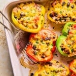 High protein stuffed bell peppers up close, a red half is being lifted out of the baking dish with a metal spatula.