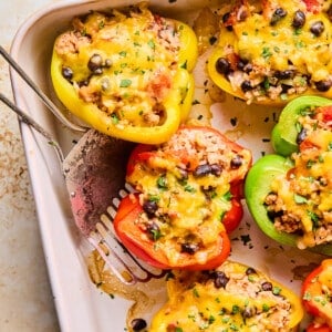 High protein stuffed bell peppers up close, a red half is being lifted out of the baking dish with a metal spatula.