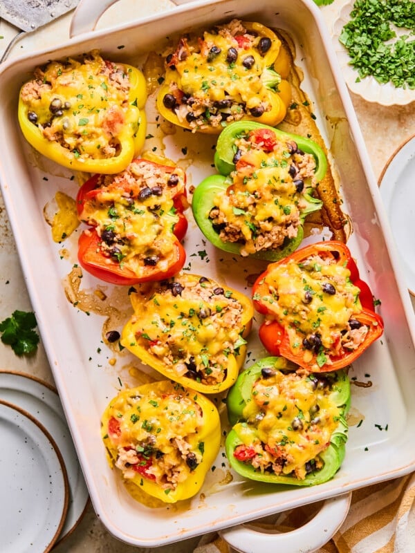 Red, green and yellow high protein stuffed bell peppers in a white baking dish on a table.