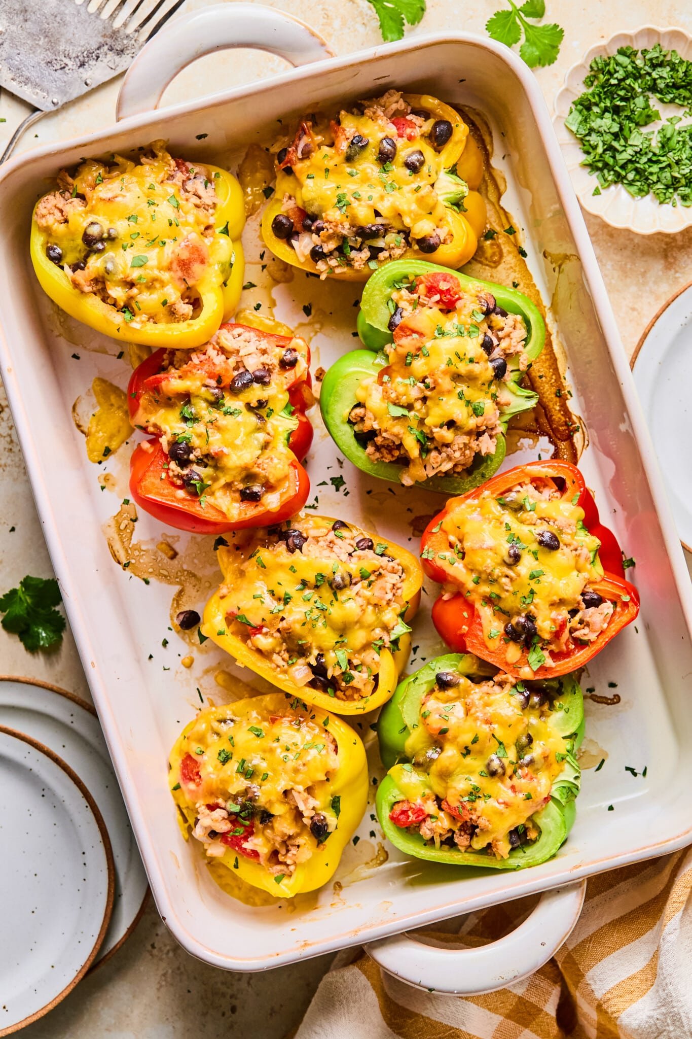 Red, green and yellow high protein stuffed bell peppers in a white baking dish on a table.