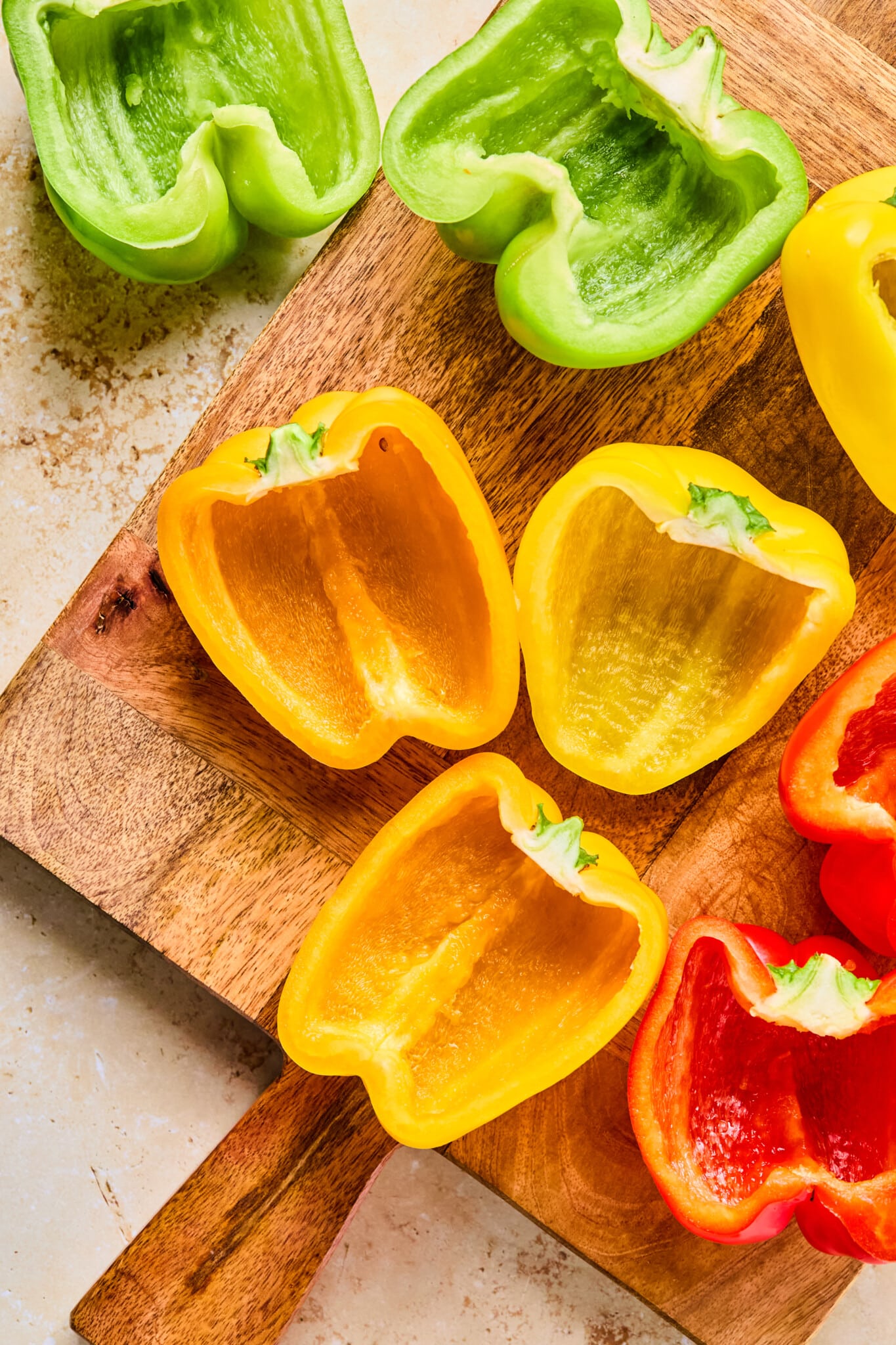 Bell peppers on a cutting board sliced in half lengthwise with pith and seeds removed.