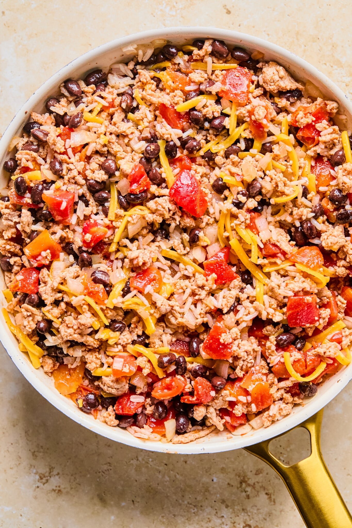 Cooked ground meat in a frying pan with diced tomatoes, beans, spices and cheese mixed in.