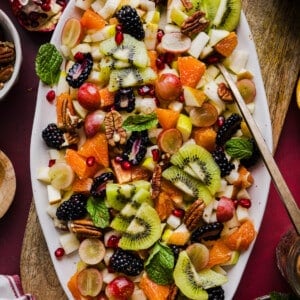 A festive and colorful thanksgiving fall fruit salad on a large white platter garnished with mint.