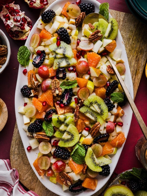 A festive and colorful thanksgiving fall fruit salad on a large white platter garnished with mint.