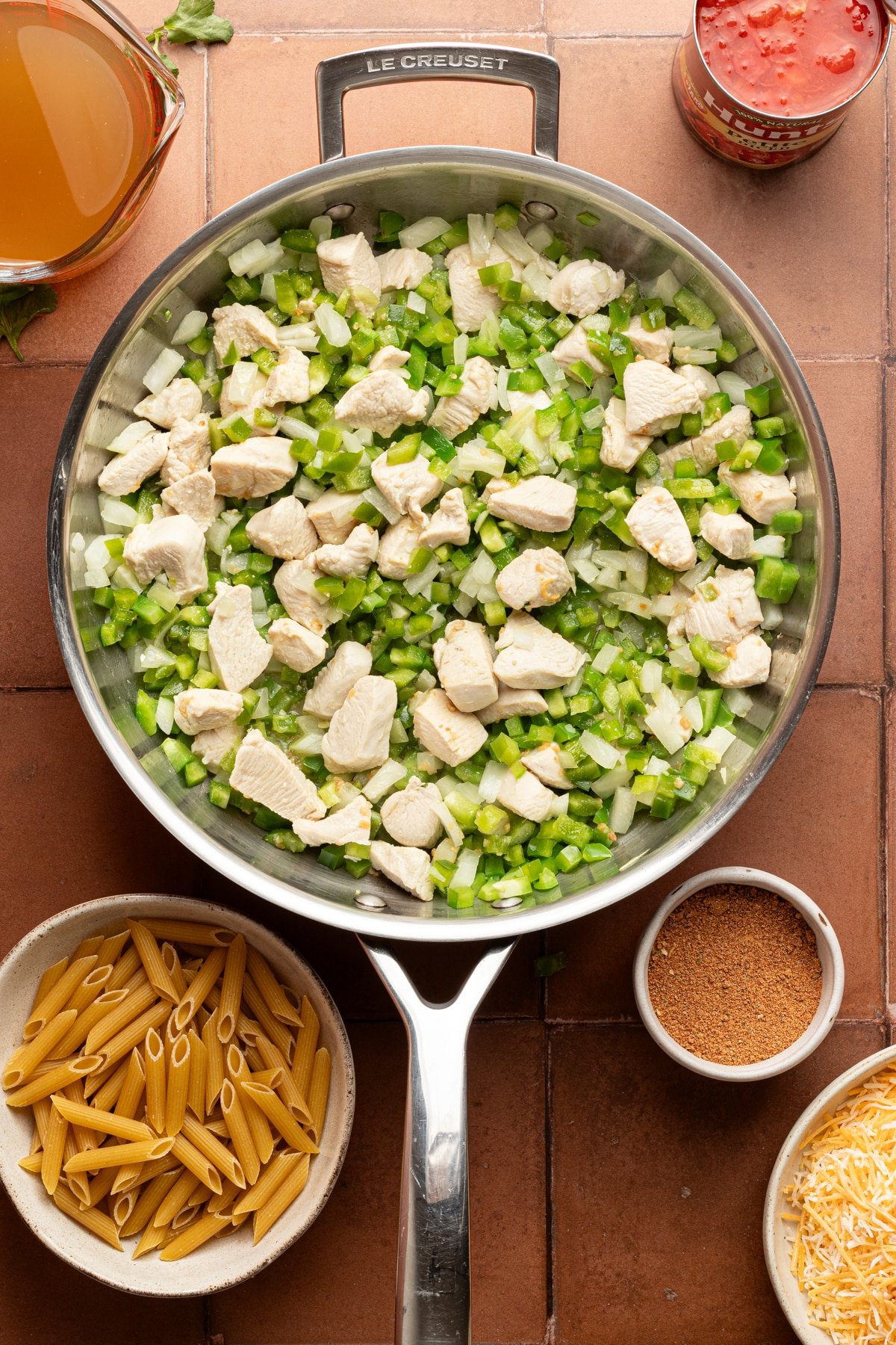 A metal skillet with diced chicken, green peppers and onions cooking.
