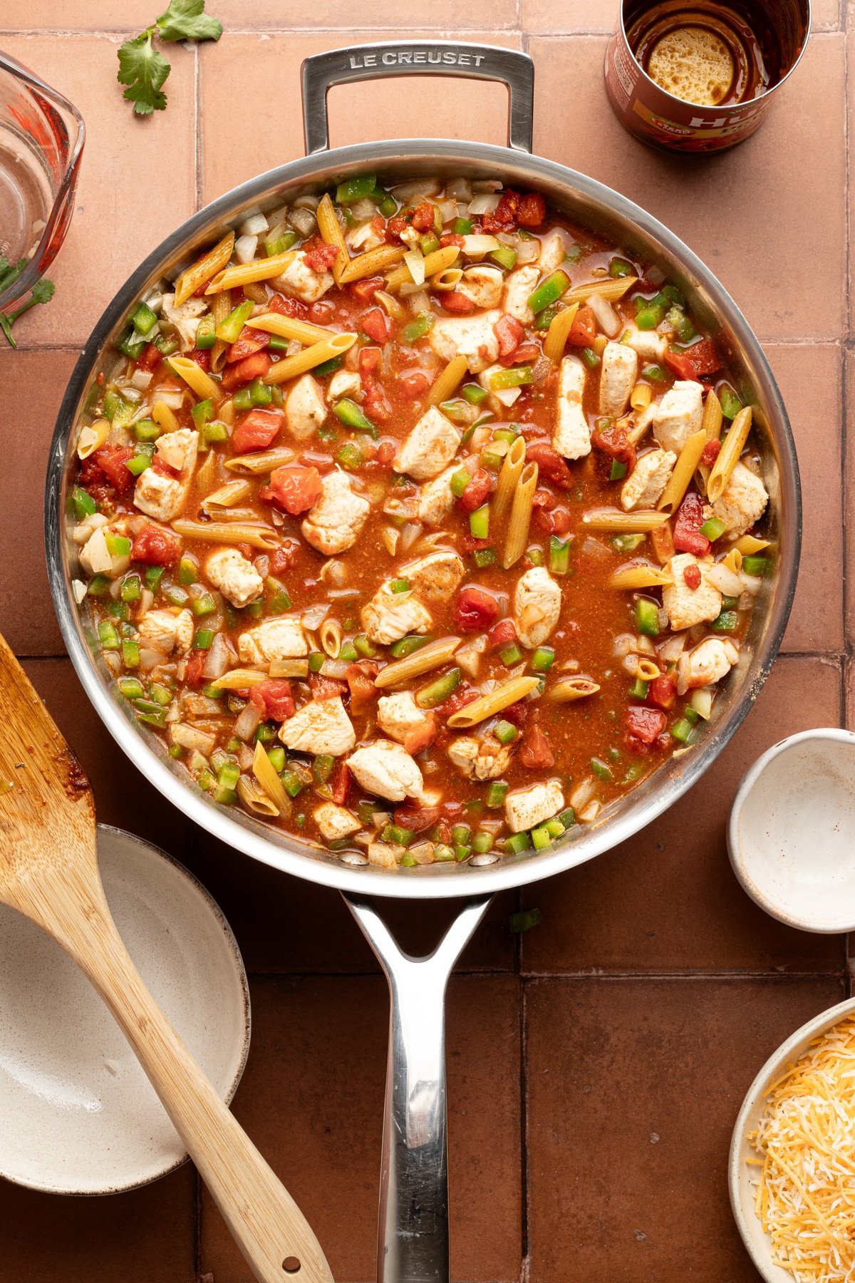 Chicken, peppers, onions, garlic, tomatoes, broth, pasta and seasoning cooking in a skillet.