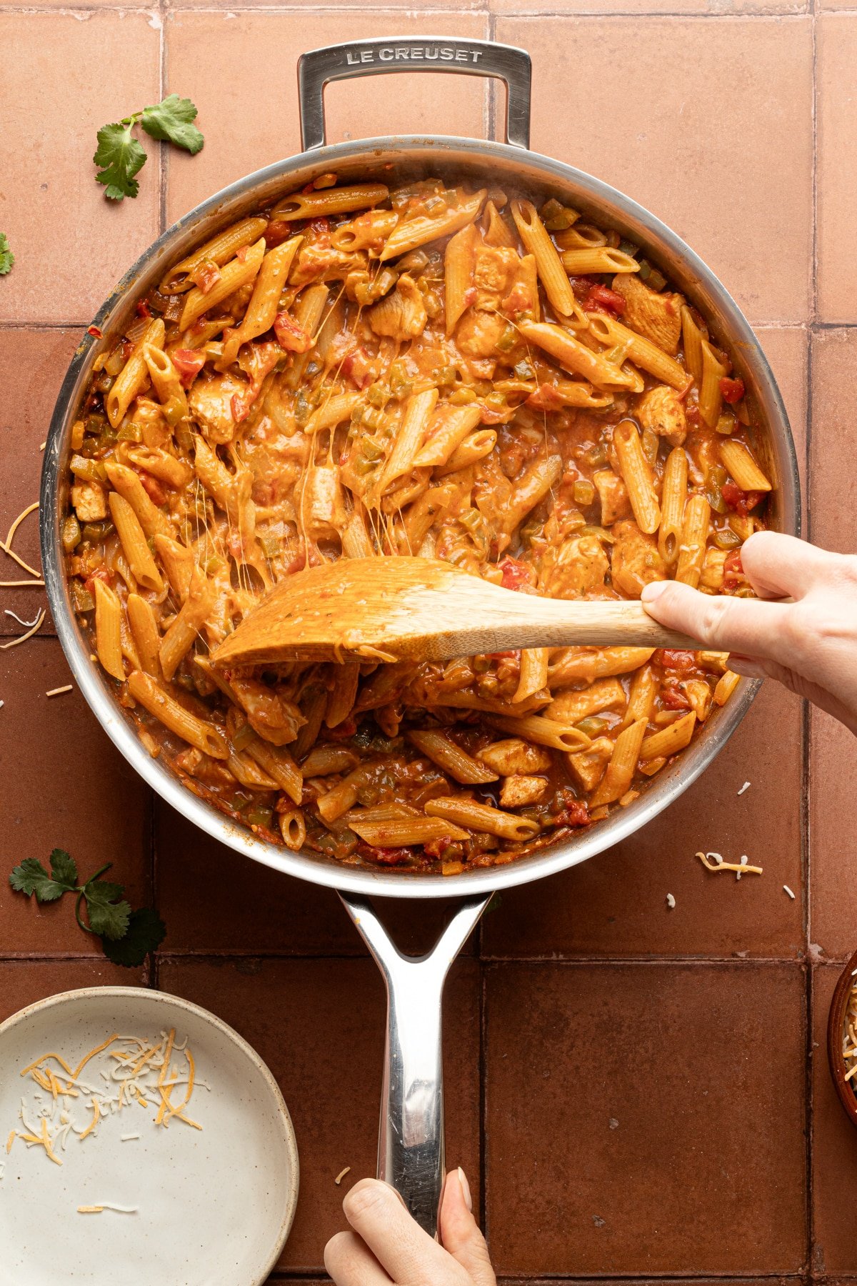 Chicken taco pasta skillet in a metal pan with melted cheese being stirred together with a wooden spoon.