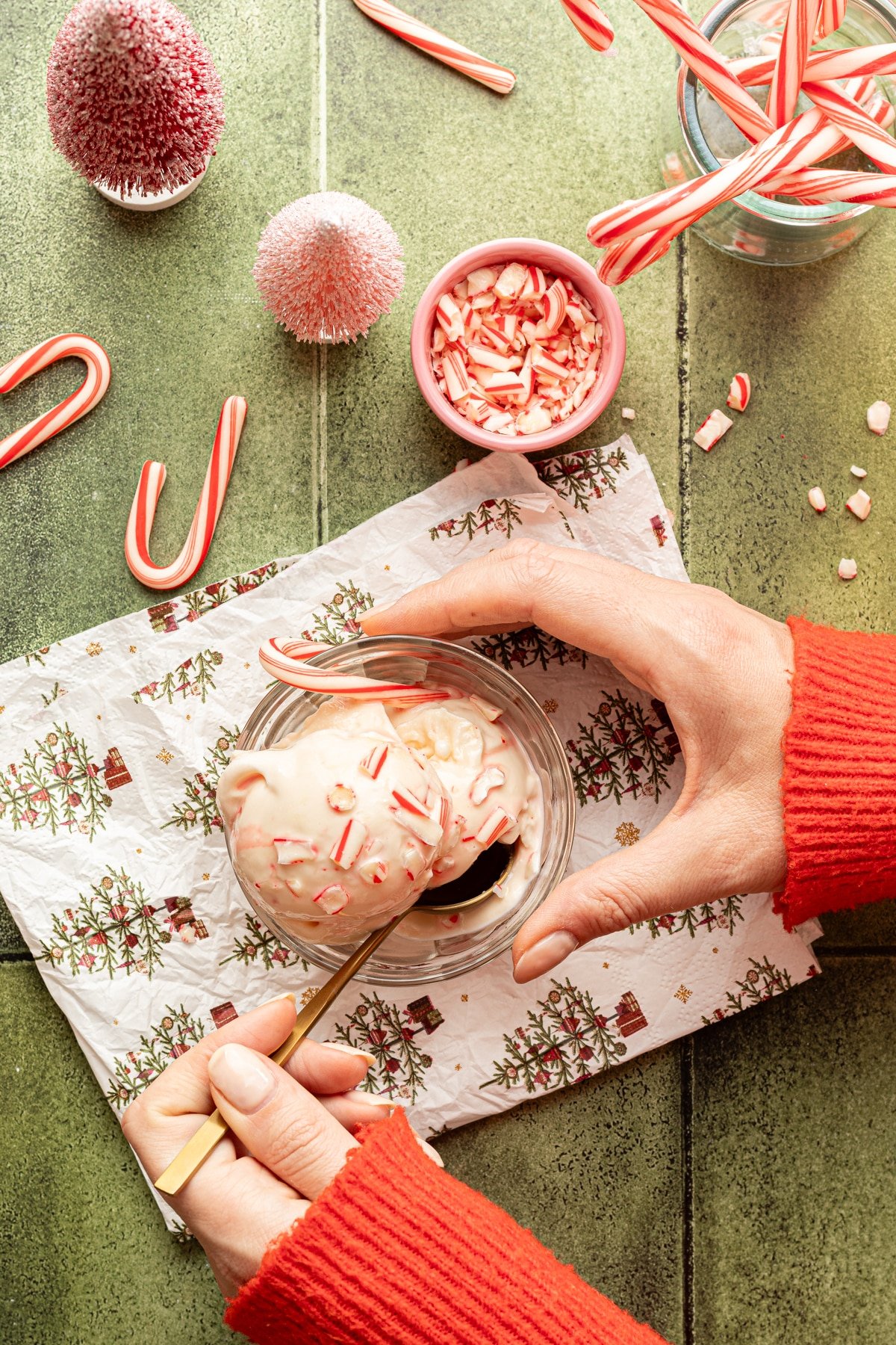 Hands holding a dish of peppermint ice cream on a Christmas tree napkin with a gold spoon.
