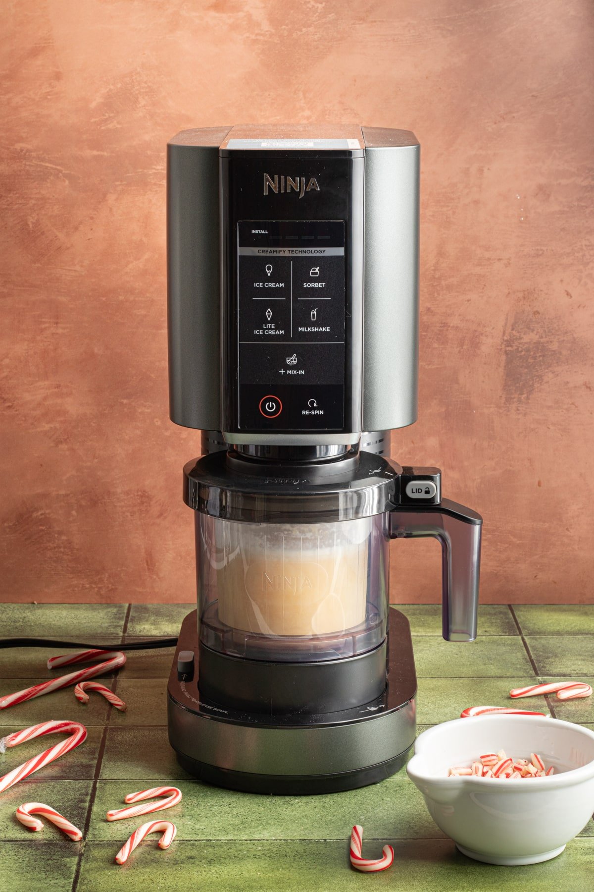 Ninja Creami ice cream machine with bowl attached to frozen peppermint ice cream base on a green counter top.