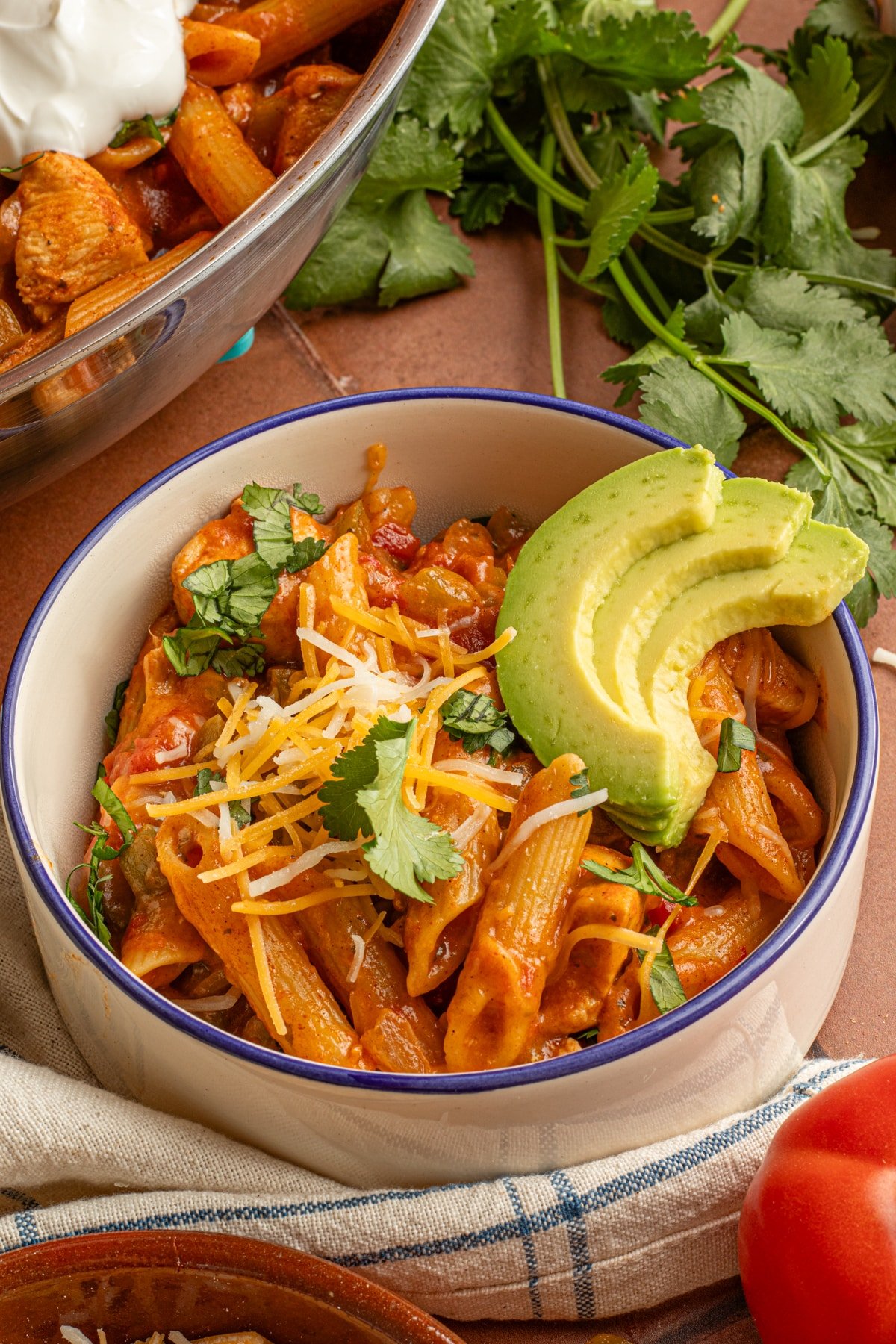 Chicken taco pasta in a bowl garnished with shredded cheese, cilantro and 3 thin avocado slices.