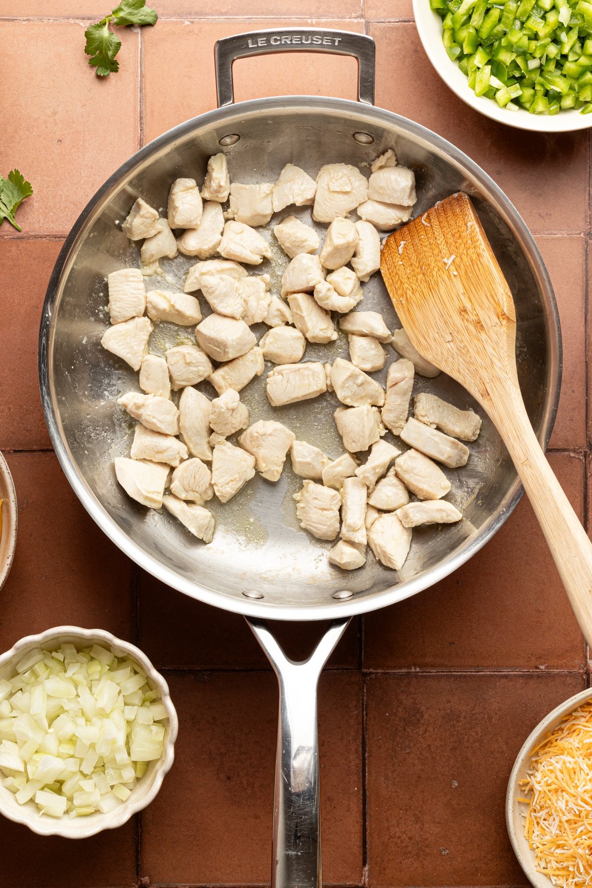 Diced chicken breast cooking in a metal skillet with a wooden spoon.