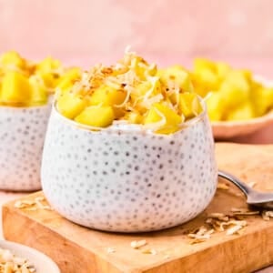 Coconut chia pudding topped with diced mango and toasted coconut displayed on a wooden board.