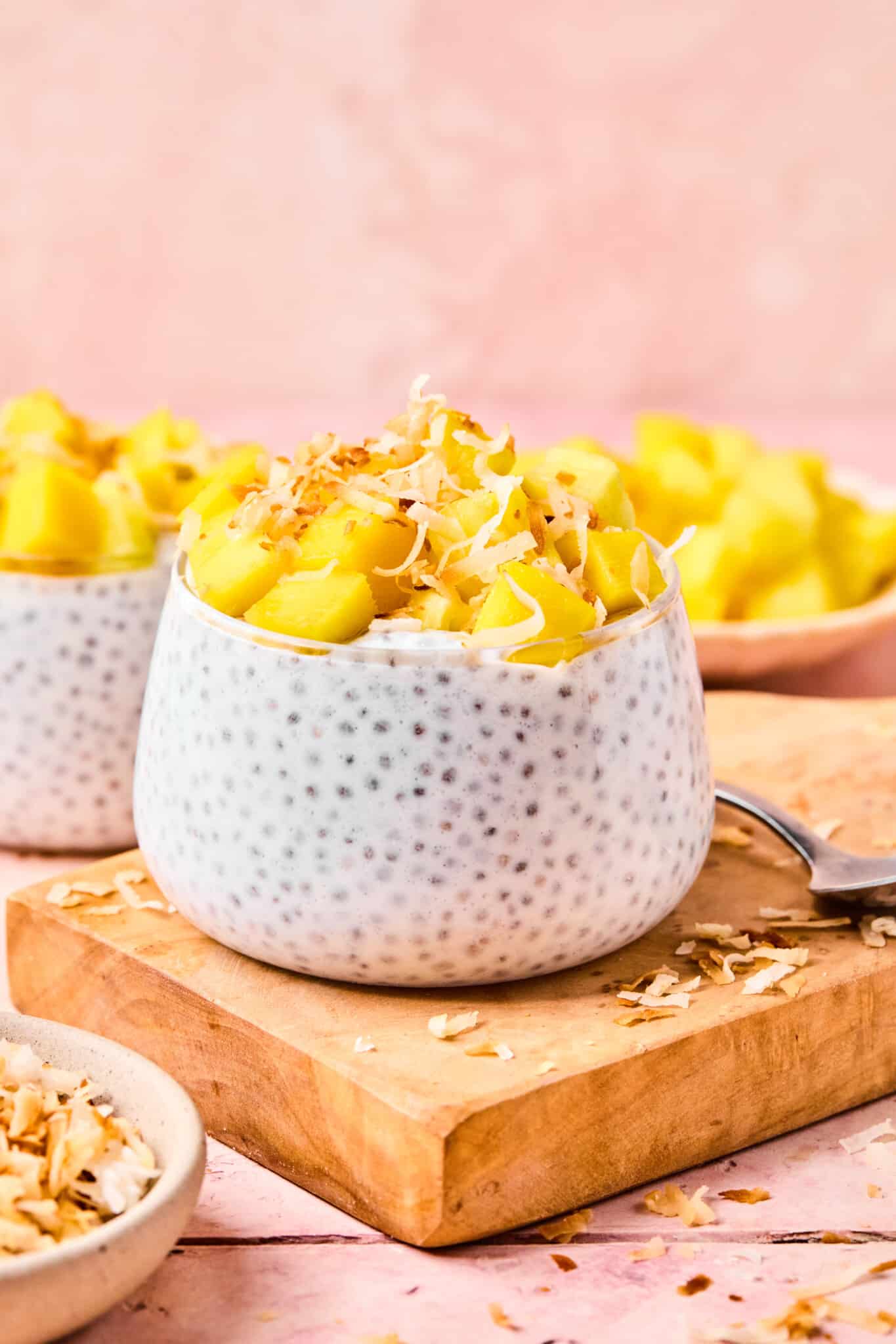 Coconut chia pudding topped with diced mango and toasted coconut displayed on a wooden board.