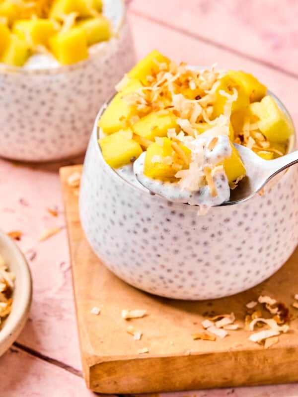 Coconut chia pudding garnished with diced mango and toasted coconut with a spoon.