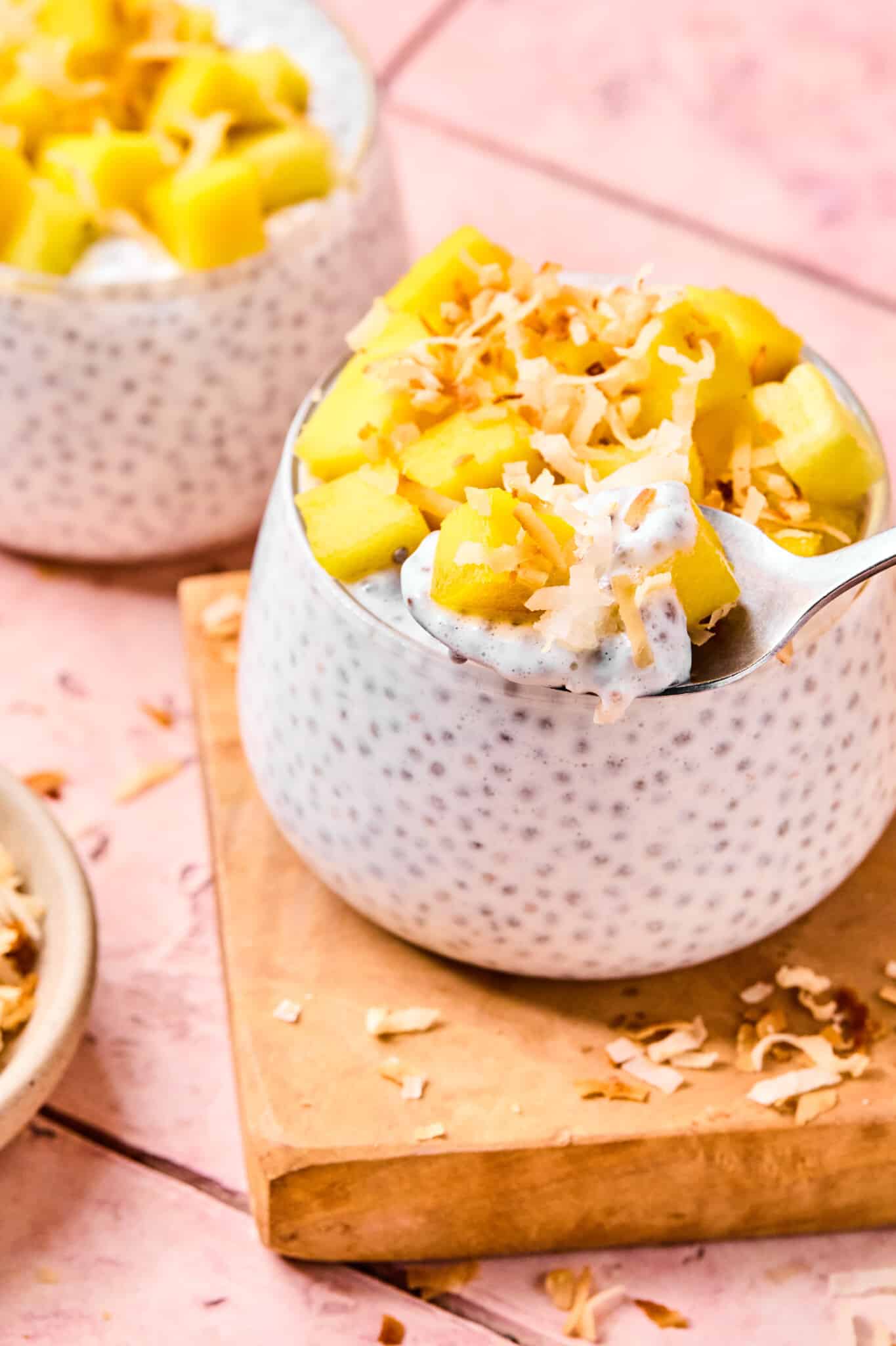 Coconut chia pudding garnished with diced mango and toasted coconut with a spoon.