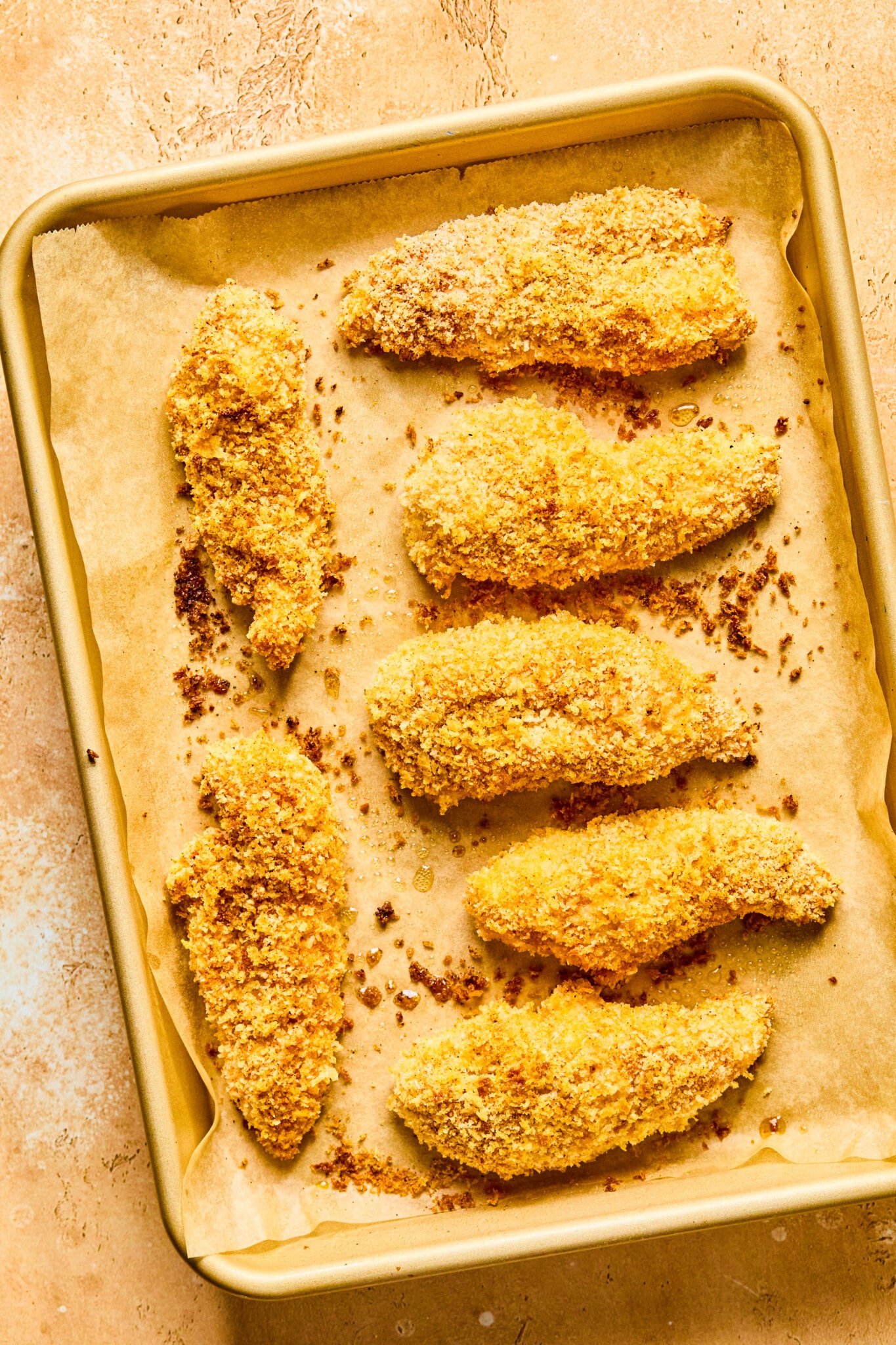 Golden brown baked chicken tenders on a parchment lined baking sheet.
