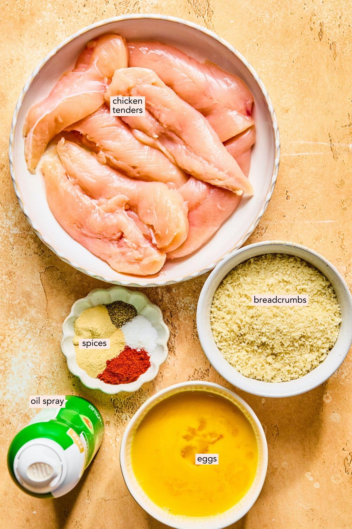 Ingredients for baked chicken tenders in bowls on a countertop.