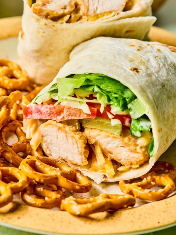 A chicken nugget wrap cut in half on a plate with pretzels.