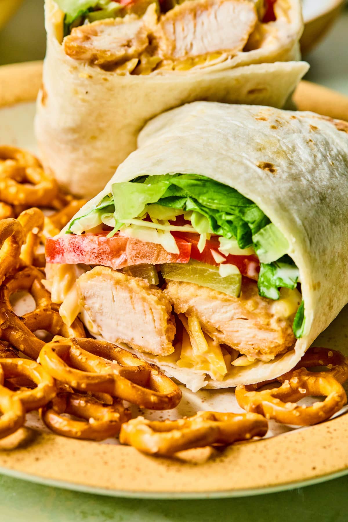 A chicken nugget wrap cut in half on a plate with pretzels.
