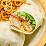 A chicken nugget wrap cut in half on a plate with pretzels.