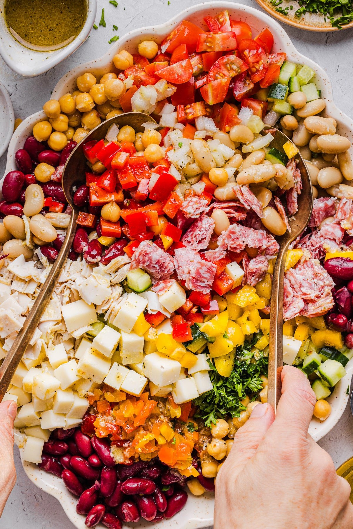 Grinder dense bean salad being mixed by two large spoons.