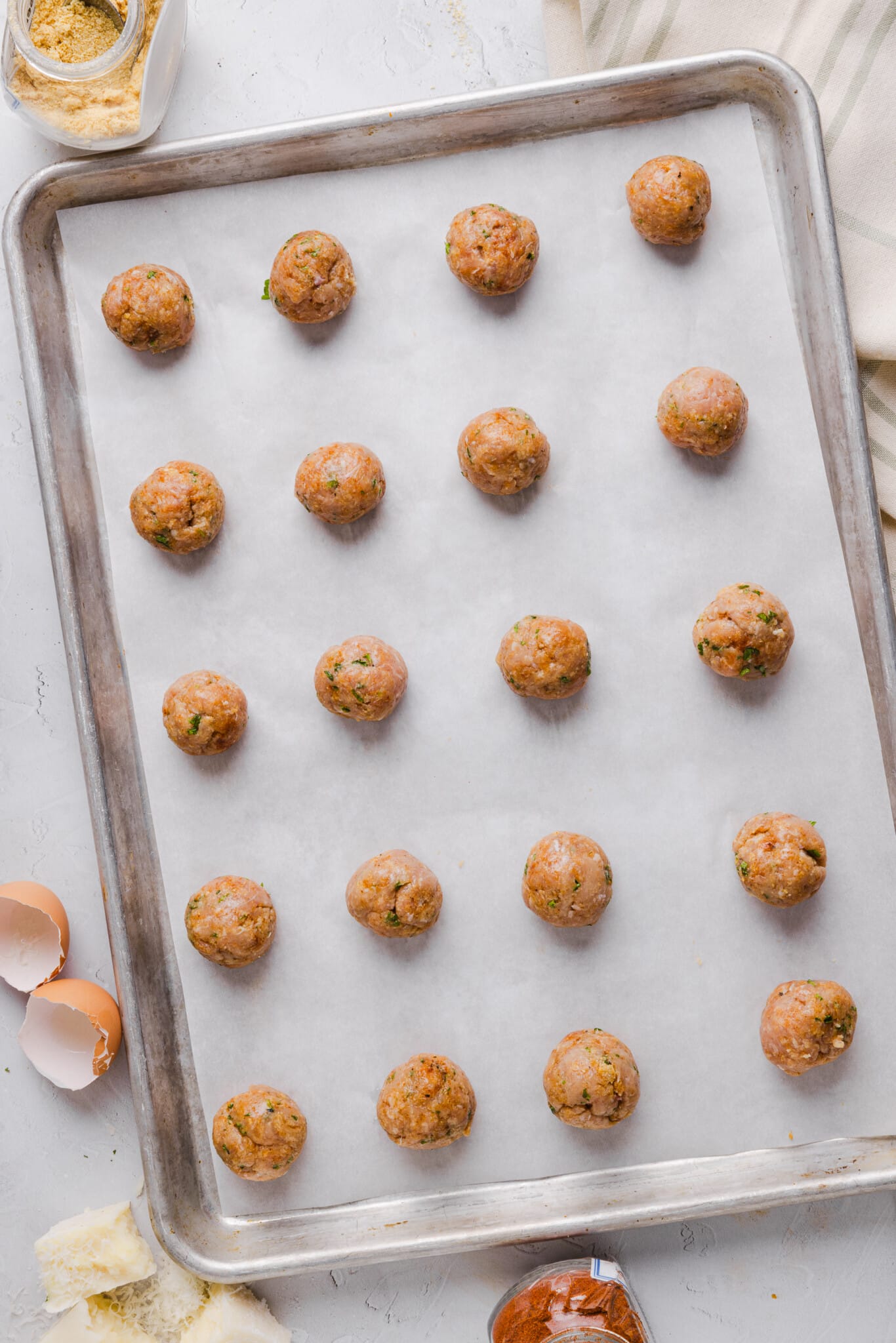 Twenty ground chicken meatballs on a baking sheet ready for the oven.