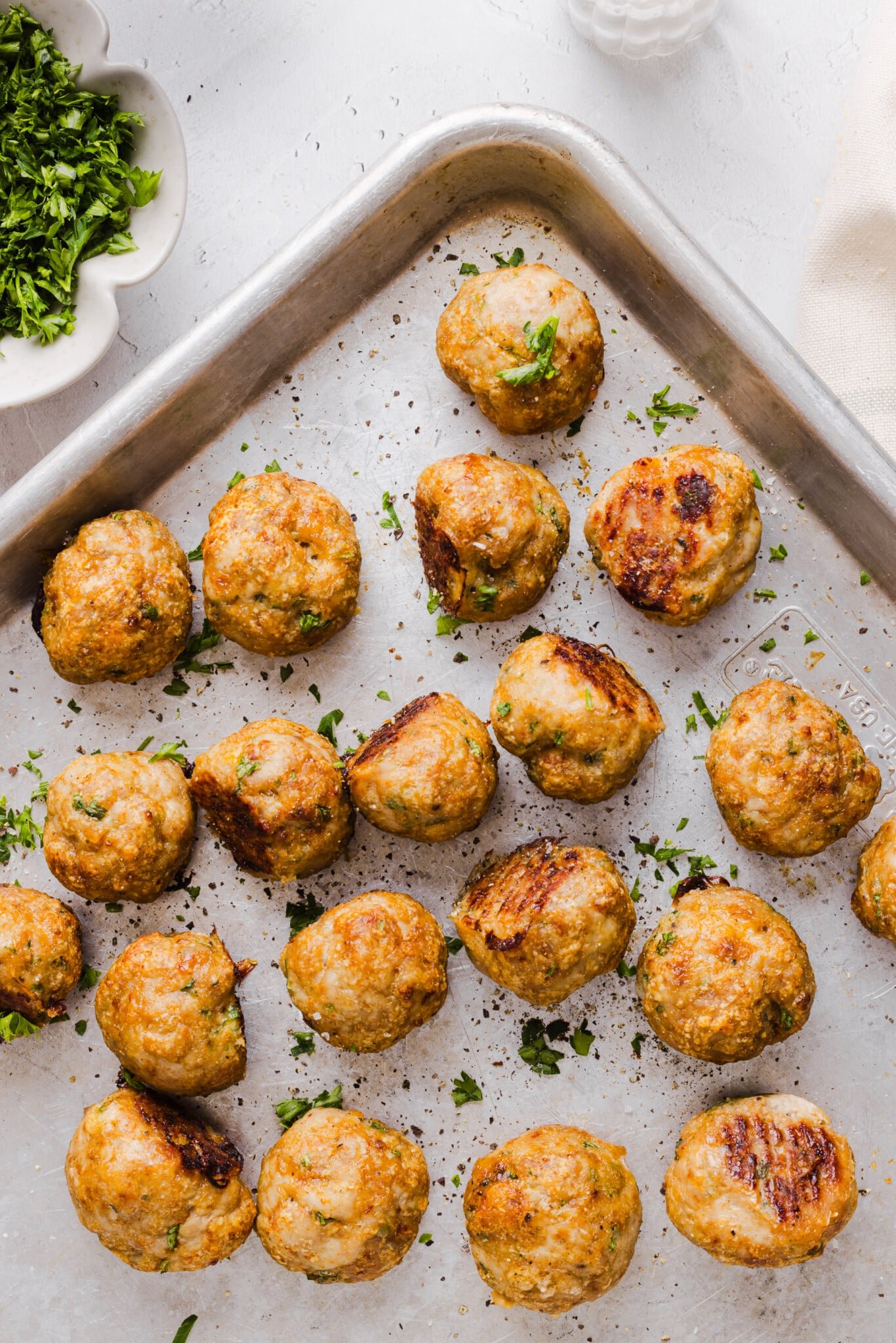 Baked ground chicken meatballs in the corner of a baking sheet garnished with chopped fresh parsley.
