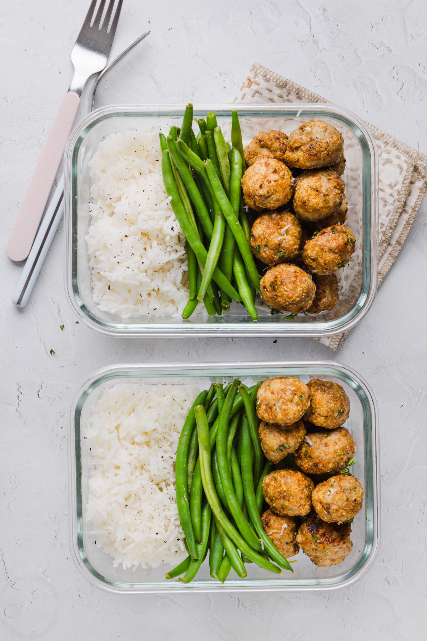 Two clear glass containers with rice, green beans and ground chicken meatballs for meal prep.