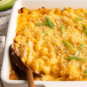 Baked high protein buffalo chicken mac and cheese with a wooden spoon garnished with sliced scallions.