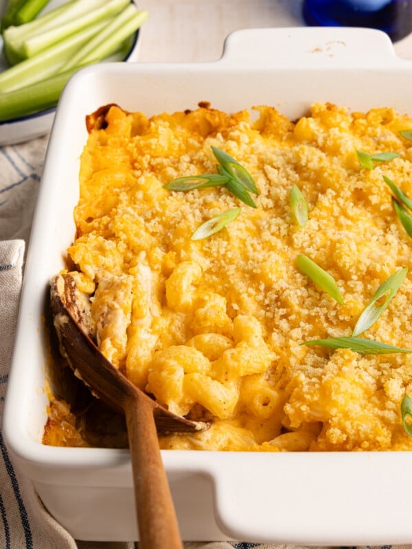 Baked high protein buffalo chicken mac and cheese with a wooden spoon garnished with sliced scallions.