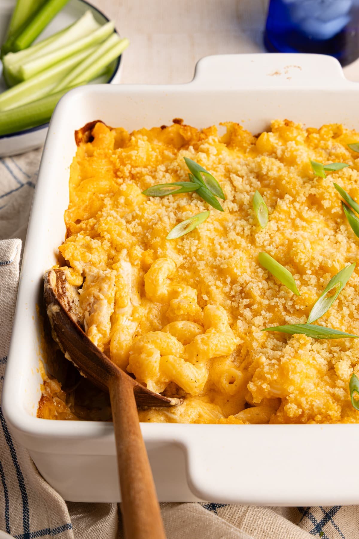 Baked high protein buffalo chicken mac and cheese with a wooden spoon garnished with sliced scallions.
