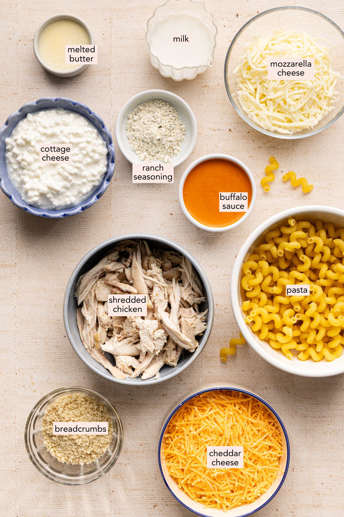 Ingredients for high protein buffalo chicken mac and cheese in individual bowls with labels.