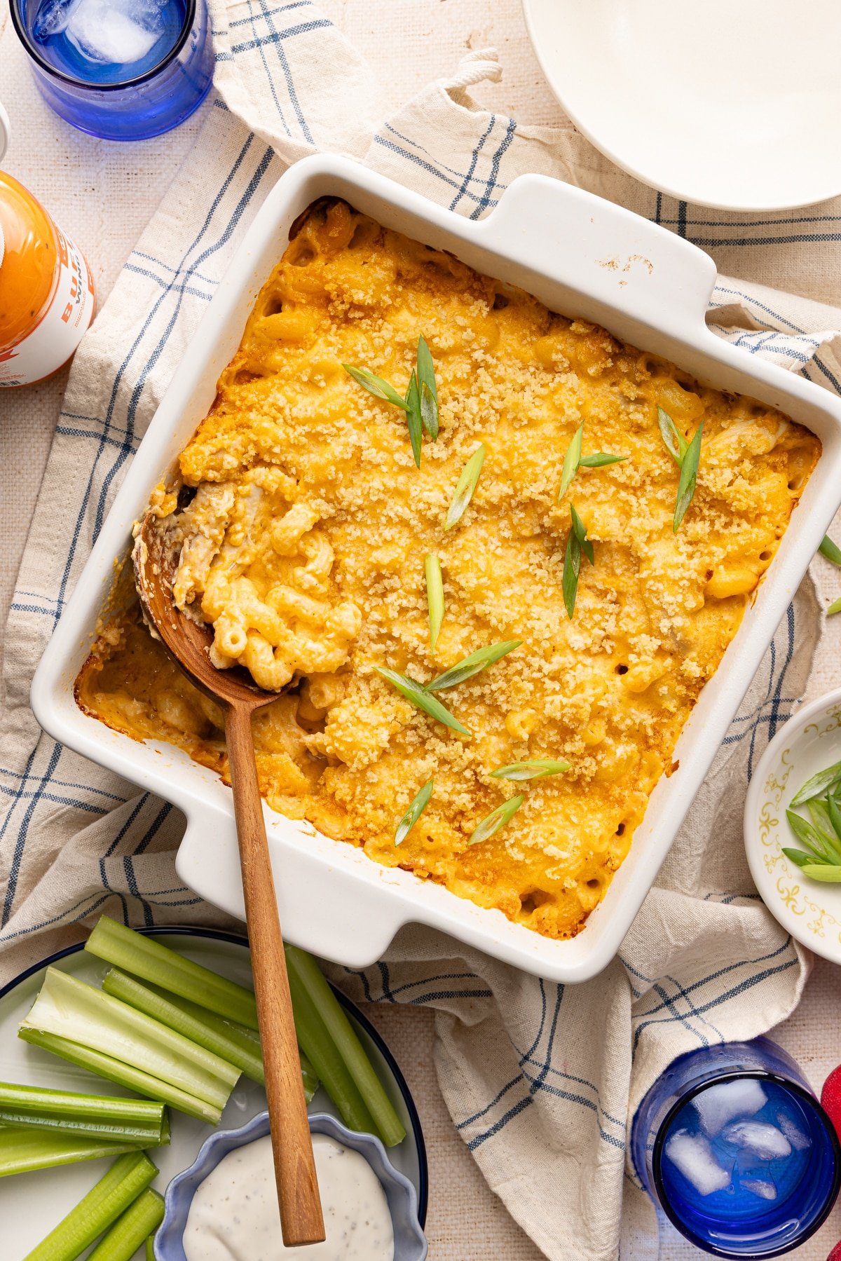 Baked high protein buffalo chicken mac and cheese with a wooden spoon garnished with sliced scallions.